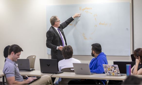 Provost Haggerty pointing to material on a whiteboard in a classroom with students