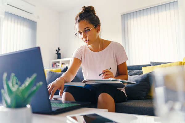 student sitting on a couch with notebooks and a laptop