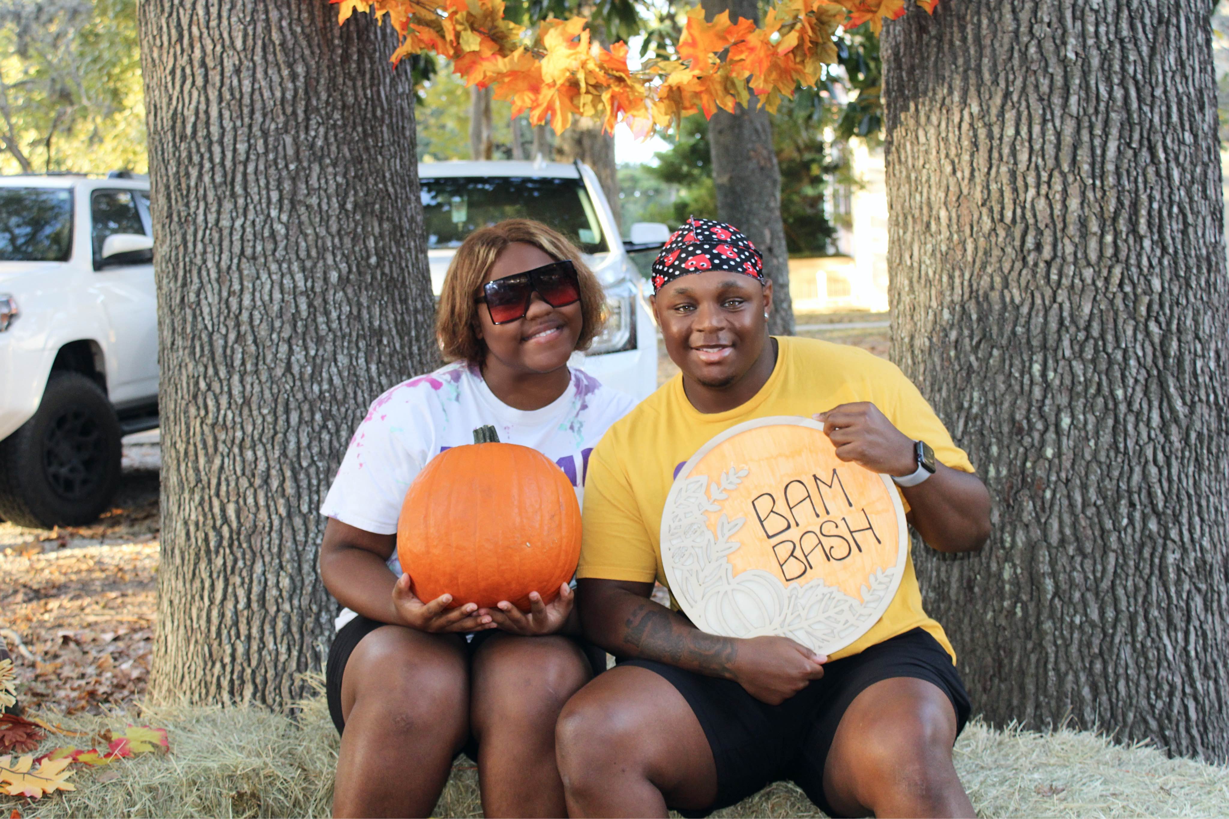 Students posing for a picture while holding a pumpkin and a sign that says BAM Bash.